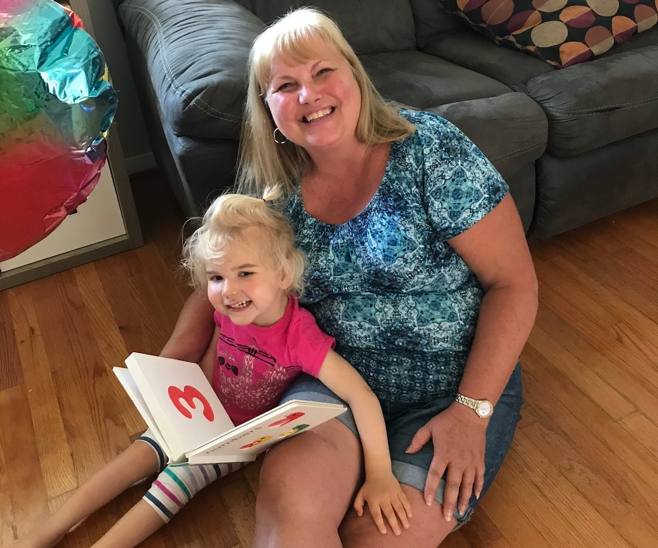 A woman smiling while sitting on the floor with a girl holding a picture book.
