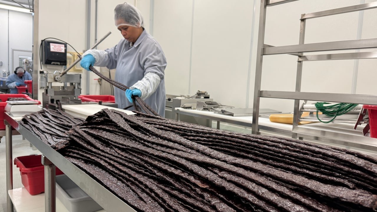 A woman in protective wear holds long strands of brown material.