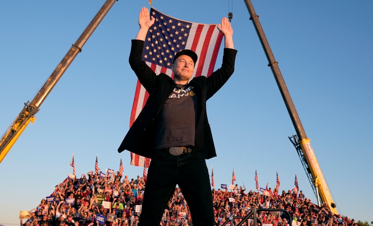 default-179 A man stands with his hands up and an American flag and a crowd on bleachers visible behind him.